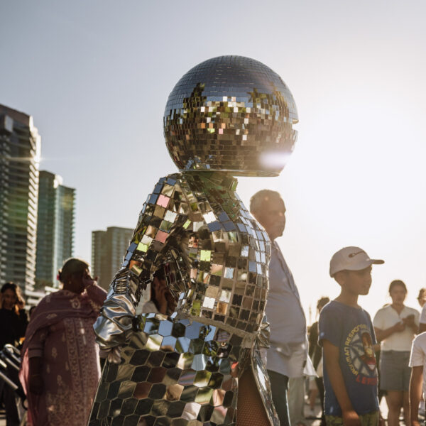 Foreground shows performer wearing full head to toe disco ball costume, with other people in the background